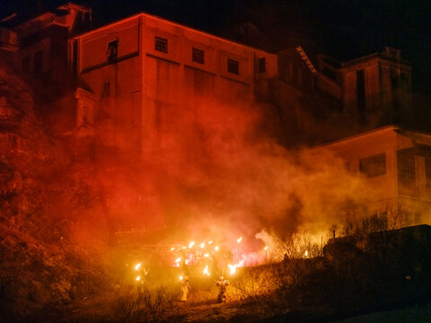 Night shot of Krampus figures holding torches, smoke and fire in front of a large building. Krampus and St Nicholas, 5 December in mining village of Cave del Predil, Tarvisio, Italy.