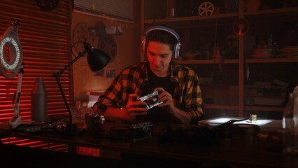 Young Man with Headphones Examining Camera in Retro Photography Studio