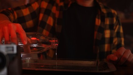 Person Pouring Liquid from Glass Bottle on Dimly Lit Table