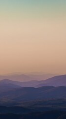 Fototapeta premium Serene sunset landscape view with soft hues over layered rolling hills and distant mountains under a calm sky, creating a peaceful atmosphere for relaxation
