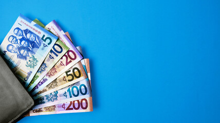 Men wallet with all Legal tender Ghanaian Cedis money currency notes as of 2025 on blue background with copy space for text
