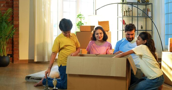 Indian family unboxing at new home, Asian young father, mother two kids eagerly taking out belongings from box while celebrating joyous moments together in their lavish new residence with smiles
