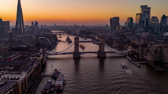 Aerial hyperlapse view of the illuminated Tower Bridge and City skyline of London during a beautiful evening with river and street traffic