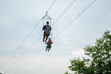 Man and woman ride on zipline, sliding on steel cable, looking at tourist picturesque green...