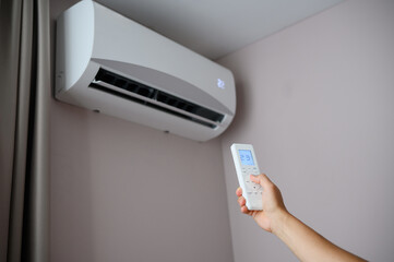 Man holds remote control in front of an air conditioner, adjusting its temperature. Man sets air...