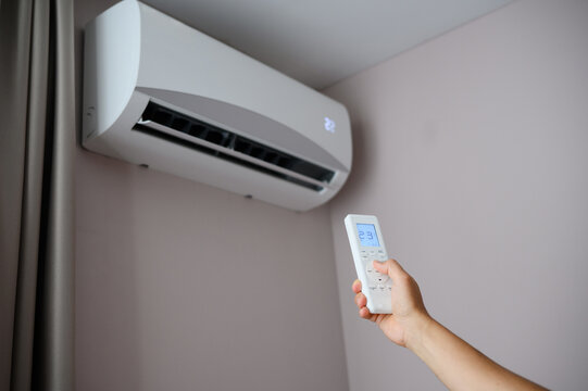 Man holds remote control in front of an air conditioner, adjusting its temperature. Man sets air conditioner to comfortable temperature of 22 degrees Celsius