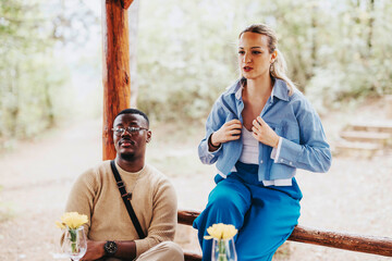 Two people enjoy a casual conversation in an outdoor setting surrounded by nature. The scene...