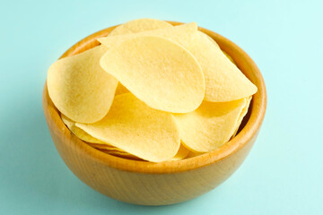 Tasty potato chips in bowl on light blue background, closeup