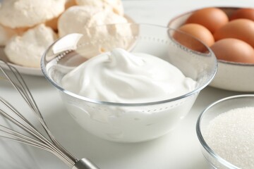 Whisk, whipped cream in bowl and other ingredients on light table, closeup. Cooking meringue cookies