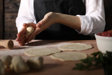 Making khinkali. Woman shaping piece of dough at table in kitchen, closeup