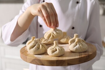 Chef holding board with uncooked khinkali indoors, closeup