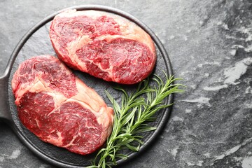 Pieces of raw beef meat and rosemary on dark table, top view. Space for text