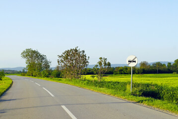 Road trip in Serbia: view of a turning asphalt road with two lanes and markings in the form of a broken line, a sign indicating the end of a no-overtaking zone and fields with cereal crops and hills