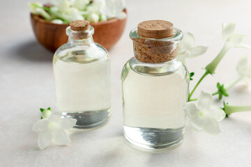 Bottles of essential oils and jasmine flowers on beige table, closeup
