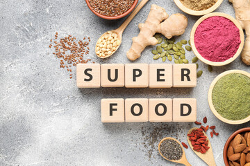 Different superfoods and words made of cubes on grey textured table, flat lay. Space for text
