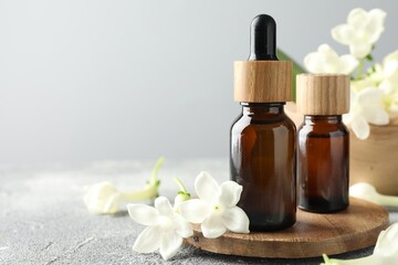 Bottles of essential oil and jasmine flowers on grey table, closeup. Space for text