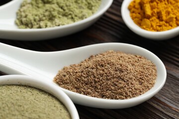 Different superfood powders in spoons on wooden table, closeup