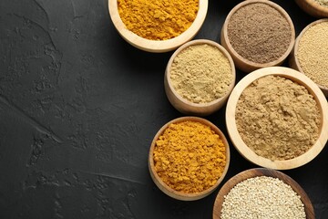 Different superfood powders in bowls on dark textured table, flat lay. Space for text