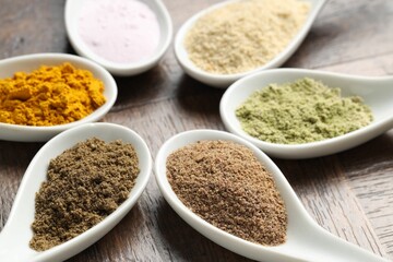Different superfood powders in spoons on wooden table, closeup
