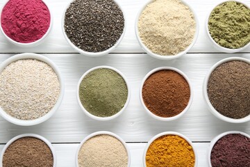 Different superfood powders in bowls on white wooden table, flat lay