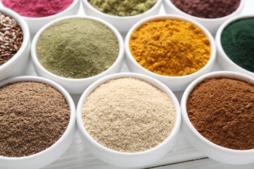 Different superfood powders in bowls on white wooden table, closeup