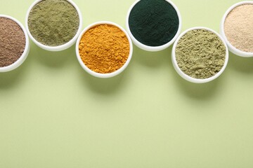 Different superfood powders in bowls on pale green background, flat lay. Space for text