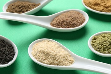 Different superfood powders in spoons on green background, closeup