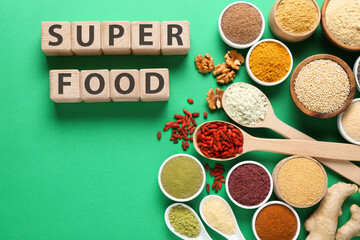 Different superfood products and words made of wooden cubes on green background, flat lay