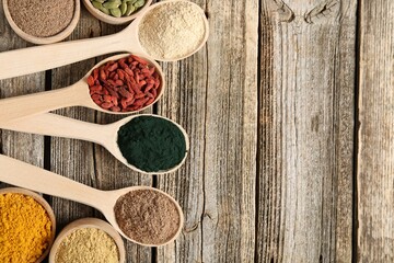 Different superfoods in spoons and bowls on wooden table, flat lay. Space for text