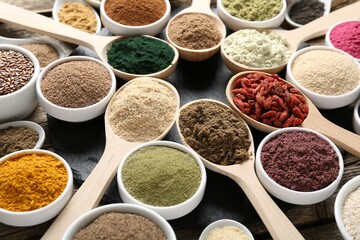 Different superfoods in spoons and bowls on table, closeup