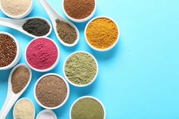 Different superfood powders in bowls and spoons on light blue background, flat lay. Space for text