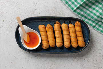 Tequeños with cheese filling, accompanied by a spicy sauce on a blue plate