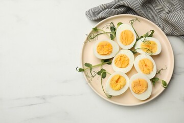 Boiled eggs, microgreens and oil on white marble table, top view. Space for text