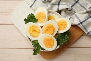 Boiled eggs and parsley in bowl on wooden table, top view