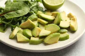 Cut ripe green avocado, greens and lime on light grey table, closeup