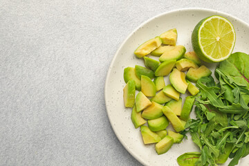 Cut ripe green avocado, greens and lime on light grey table, top view. Space for text