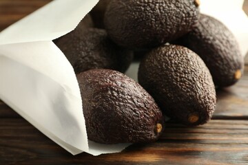 Ripe avocado fruits in paper package on wooden table, closeup