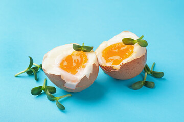 Soft boiled eggs with microgreens on light blue background, closeup