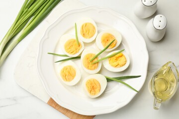 Halves of hard boiled eggs with green onions on white table, flat lay