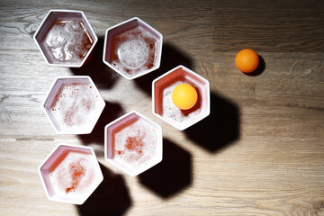 Plastic cups with drinks and balls on wooden table, flat lay. Beer pong game