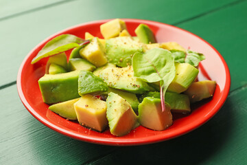Tasty cut avocados with spinach and dressing on green wooden table, closeup