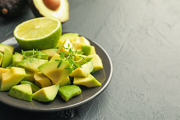 Tasty cut avocados, thyme and lime on black table, closeup. Space for text