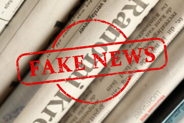 Red Fake News stamp and newspapers in different languages as background, closeup