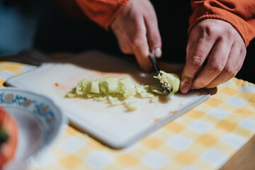 Hands expertly slicing a fresh green bell pepper with a knife, showcasing food preparation in a cozy kitchen setting, offering a sense of cooking, warmth, and culinary process.
