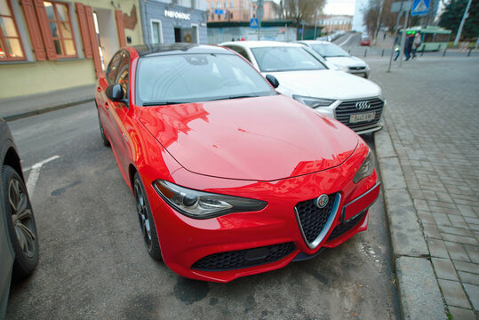 Minsk, Belarus. Dec 22, 2024. Red Alfa Romeo Giulia sedan parked close to the curb , front headlight and grille with stylish italian design. Parked Alfa Romeo Gulia on parking lot in the city