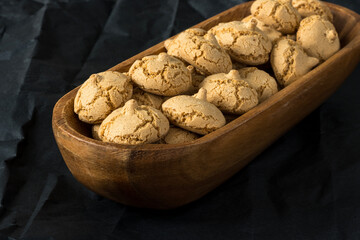 Amaretti cookie in a wooden bowl on a black background , side view , high-resolution  . Delicious , crunchy biscuits for tea .