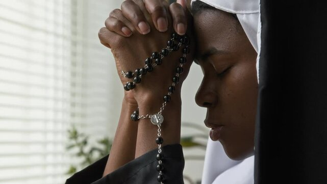 Close-up view of African American gen Z religious sister praying to god with rosary beads clasping hands together symbolizing humility and reverence