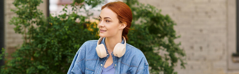 Curly red haired woman enjoying a summer stroll in the park with headphones on