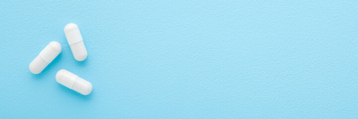 White capsule pills on light blue table background. Pastel color. Closeup. Wide banner. Empty place for text. Top down view.