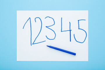 Marker and written different numbers on white paper on light blue table background. Pastel color....